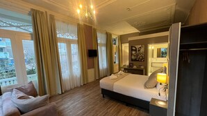 Quarto de hotel com cama, mesa de cabeceira, luminária, TV e vista para o exterior.