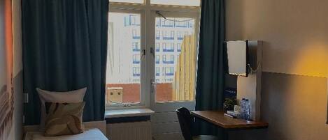 Une chambre d’hôtel avec deux lits, un bureau, une chaise et une fenêtre avec des rideaux.