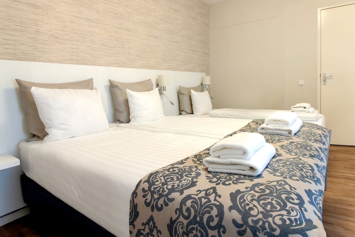 A hotel room with two beds, beige headboards, and a patterned bedspread.