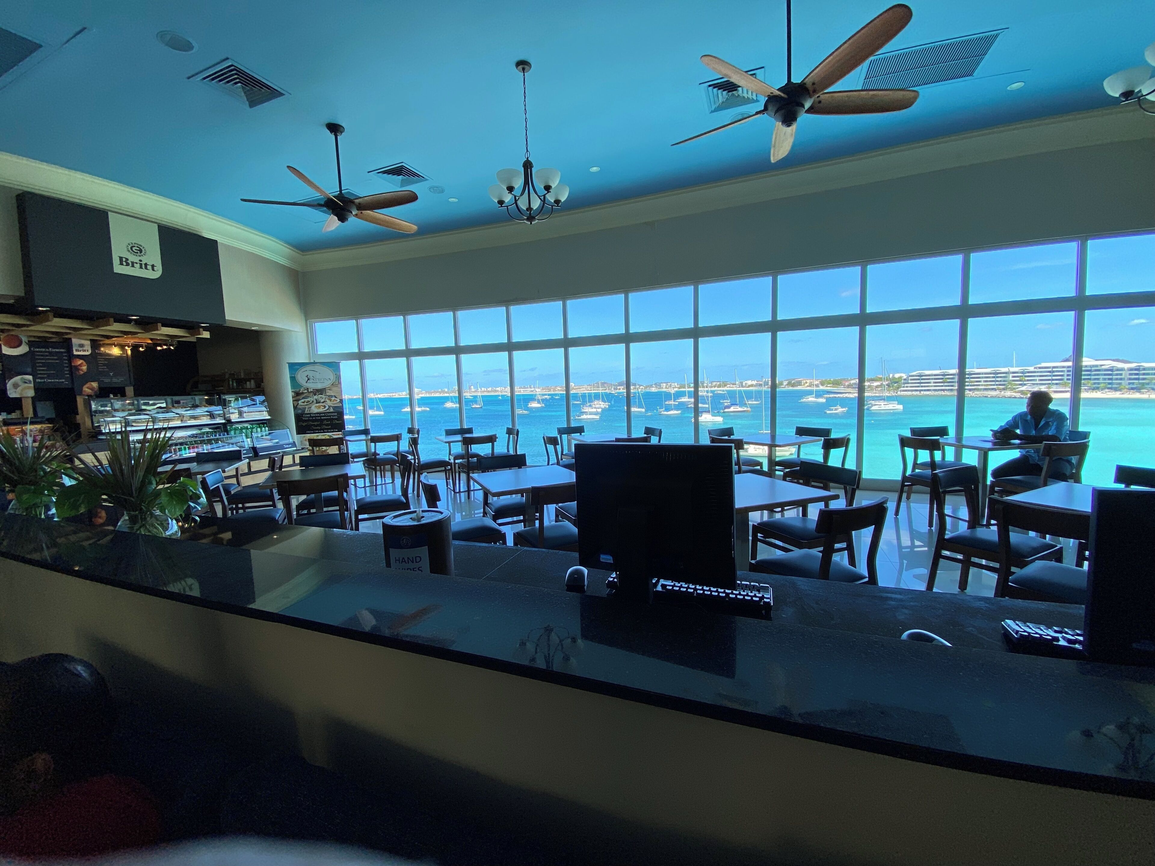 A restaurant with large windows overlooking the sea, multiple ceiling fans, and a variety of seating arrangements.