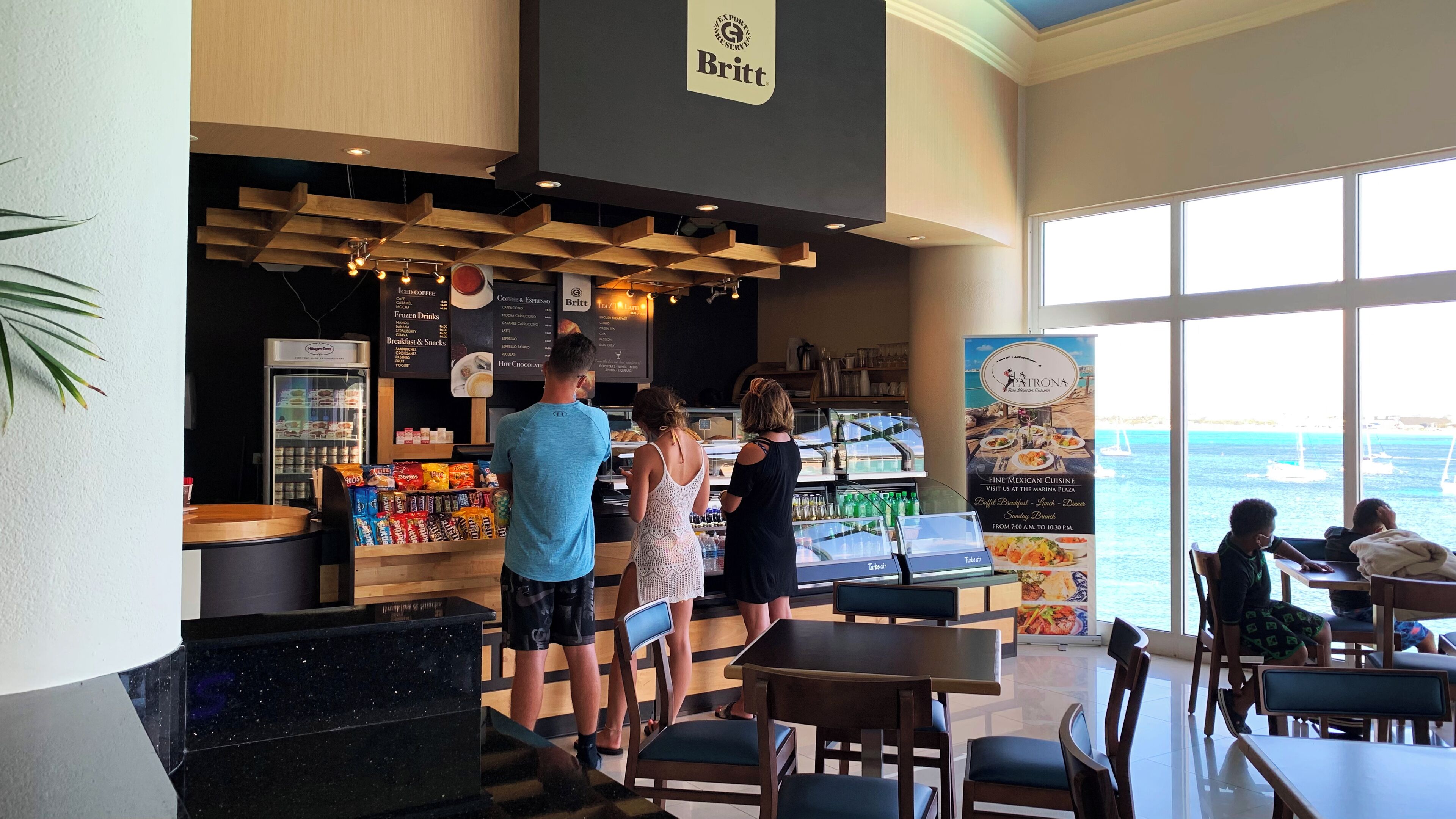 A restaurant with a menu board, a sign for 'Britt', and a view of the sea through large windows.