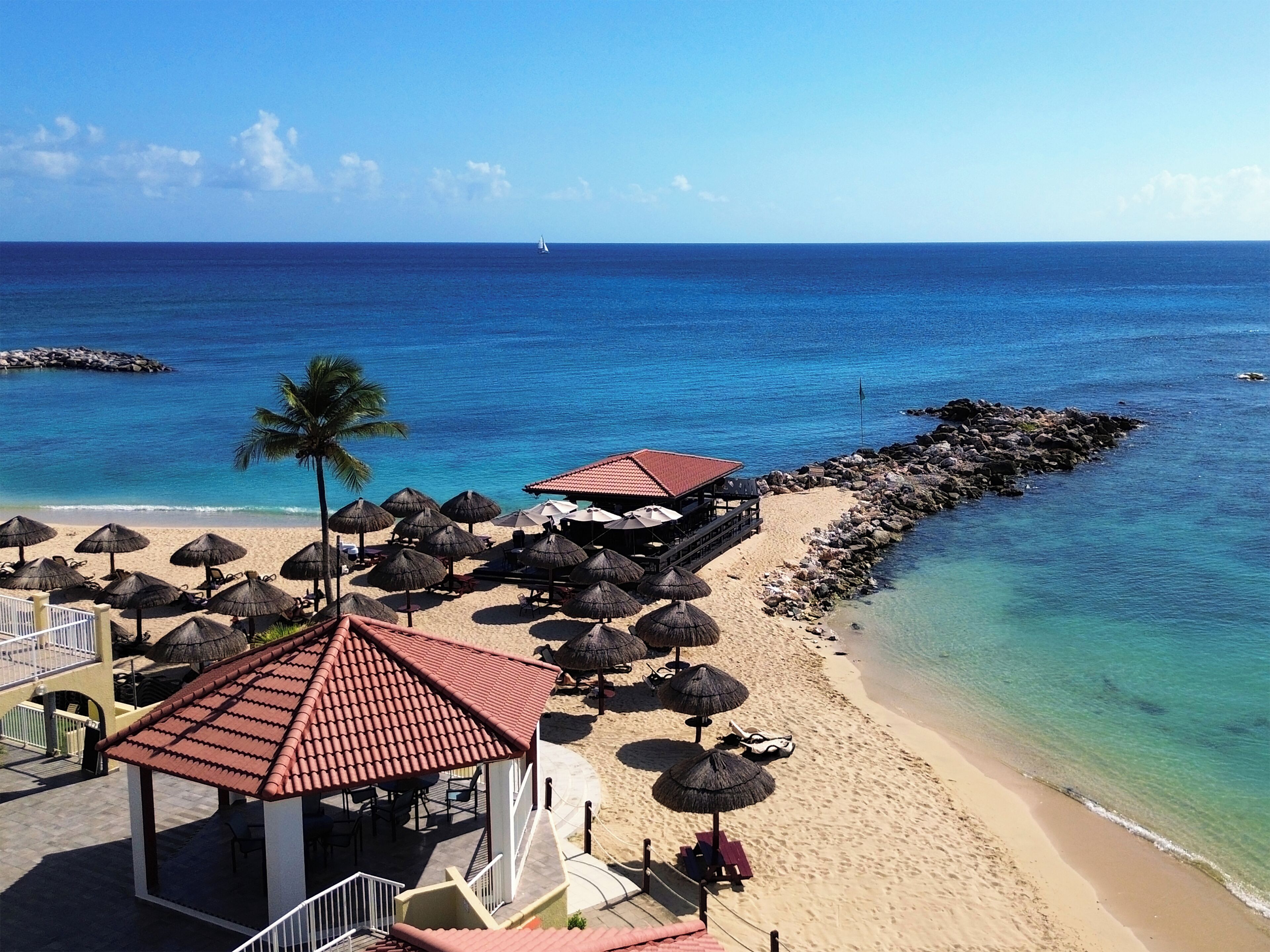 A beachside resort with a covered seating area, umbrellas, and a view of the ocean.