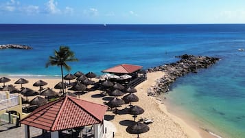 A beachside resort with a covered seating area, umbrellas, and a view of the ocean.