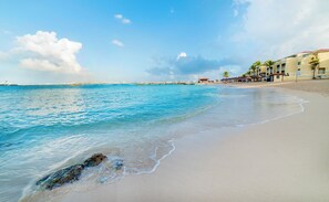 A beach with clear blue water, a sandy shore, and a row of buildings with a red roof.
