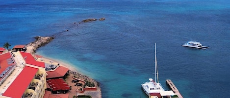 Un hotel frente al mar con un puerto deportivo, aguas azul turquesa y una isla al horizonte.