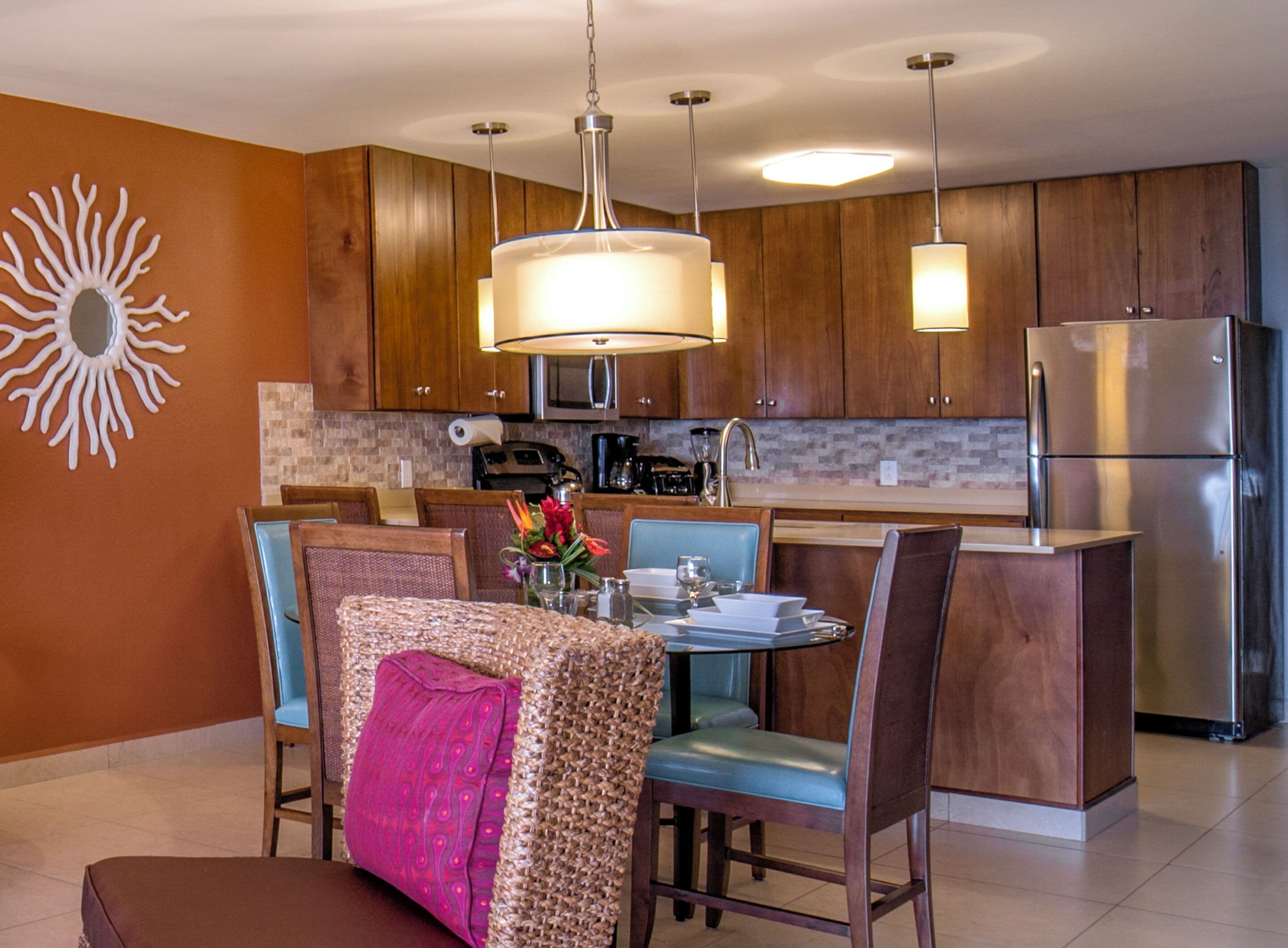 A modern kitchen with wooden cabinets, a stainless steel refrigerator, and a dining area with a table and chairs.