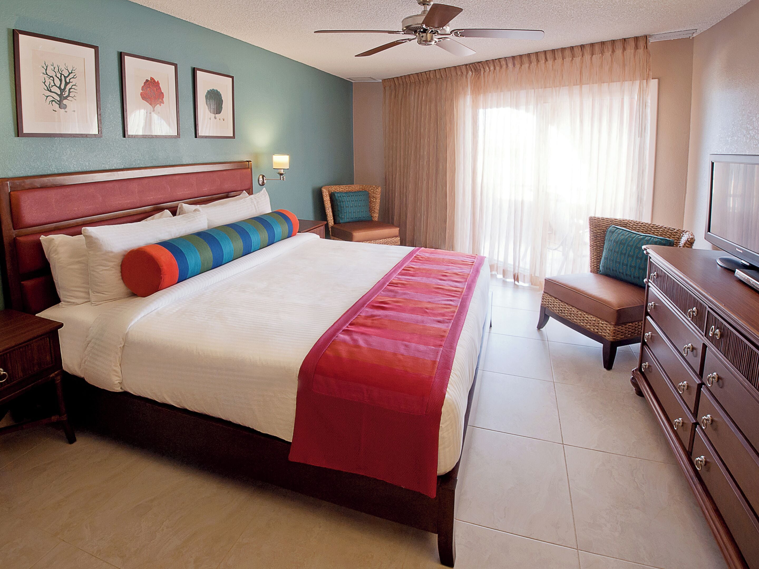 A hotel room with a large bed, a television, a dresser, and a ceiling fan.