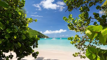 A beach with clear turquoise water, boats, and lush greenery.