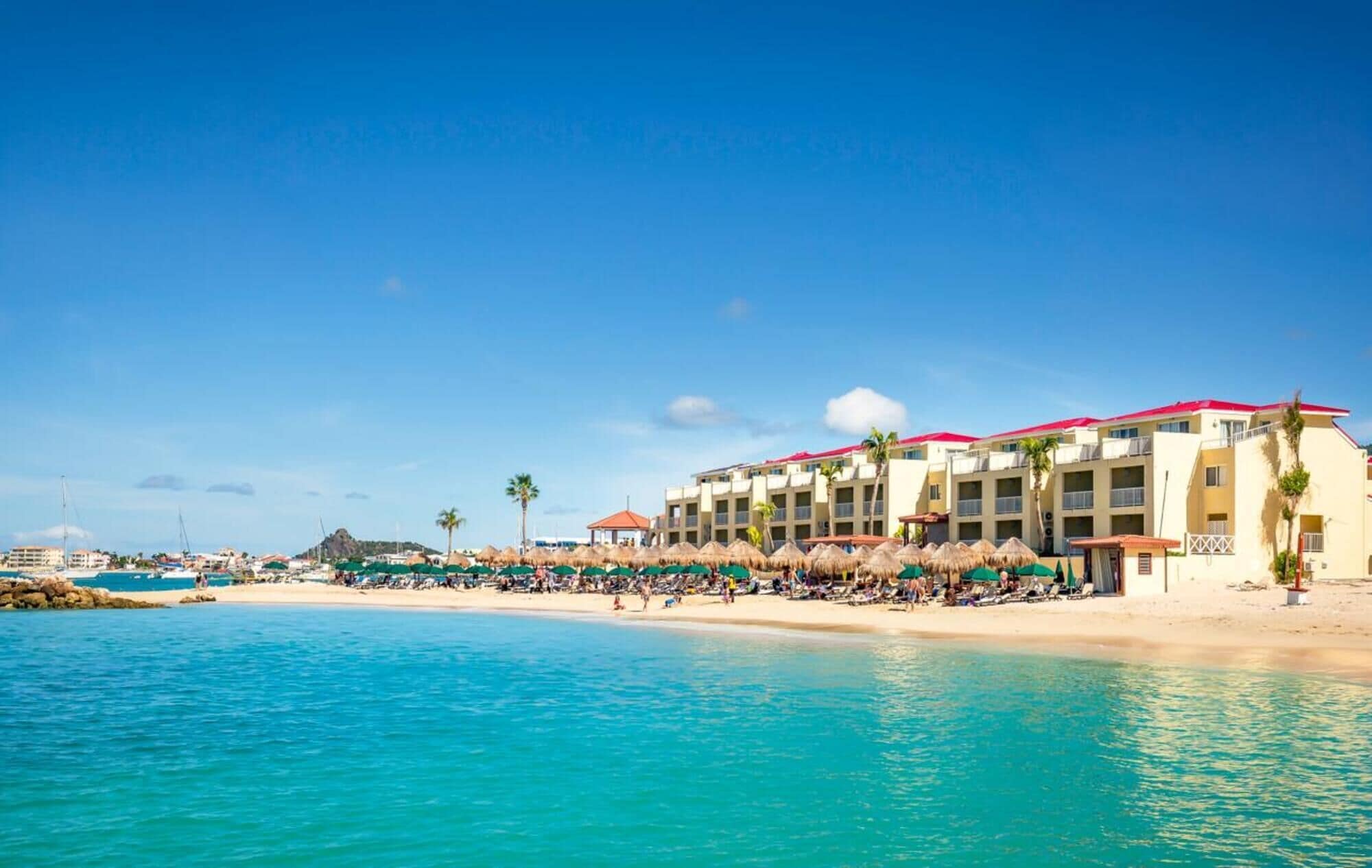 A beachfront hotel with multiple balconies, a sandy beach, and a clear blue sky.