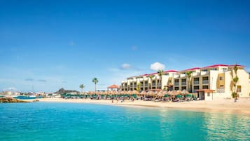 A beachfront hotel with multiple balconies, a sandy beach, and a clear blue sky.