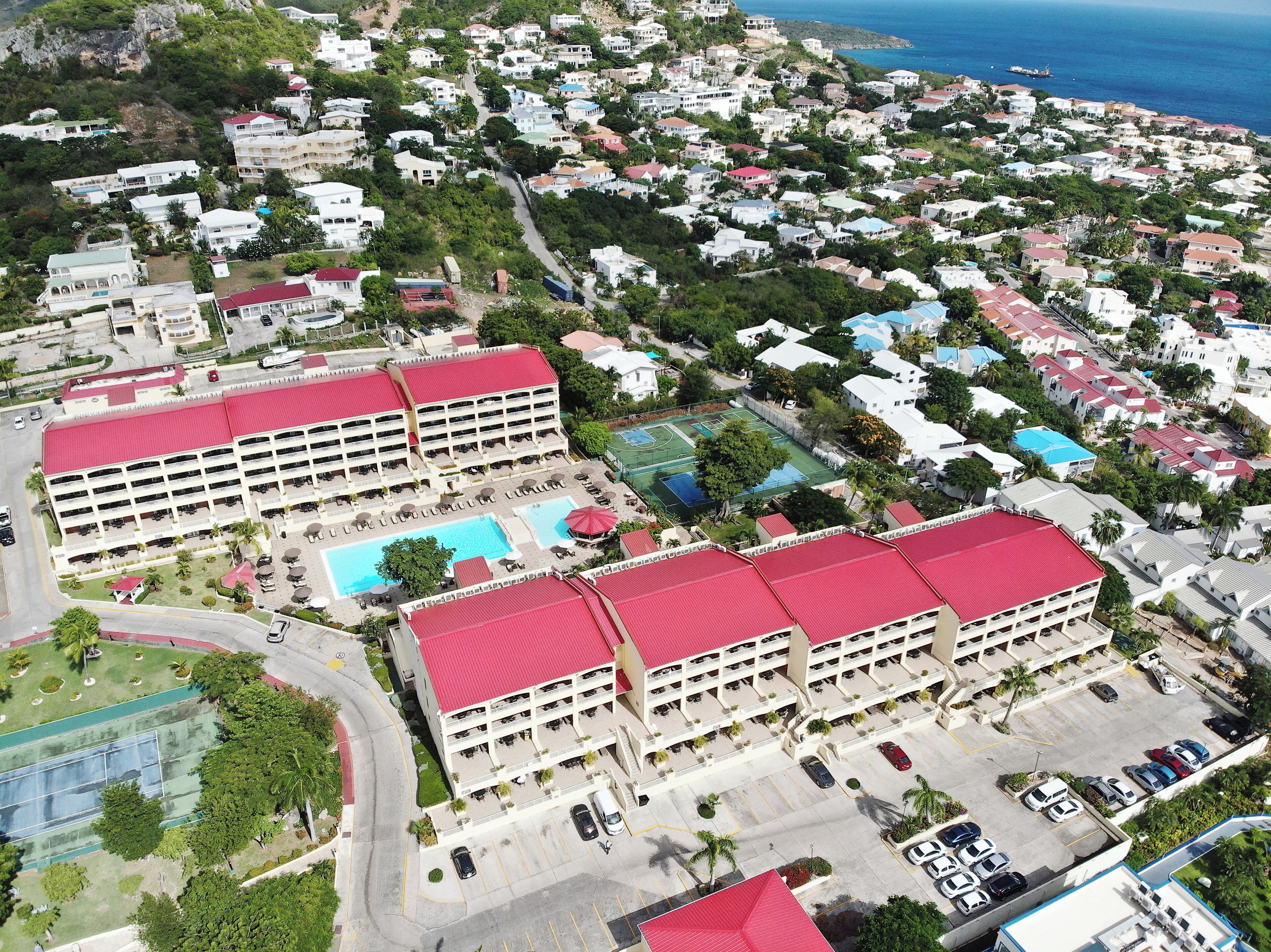 A large hotel with multiple red-roofed buildings, a swimming pool, and a tennis court.