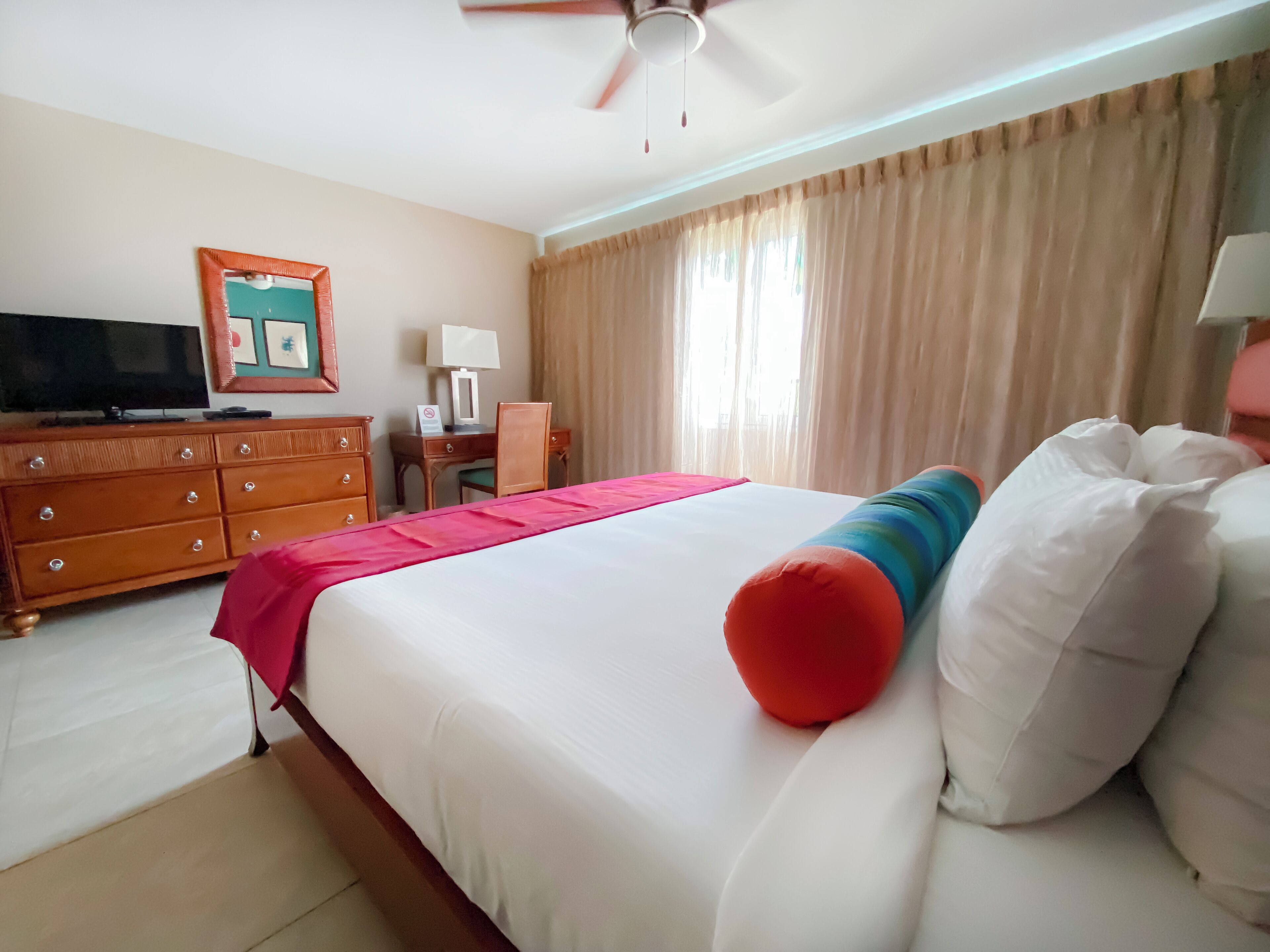 A hotel room with a bed, a desk, a television, and a window with curtains.