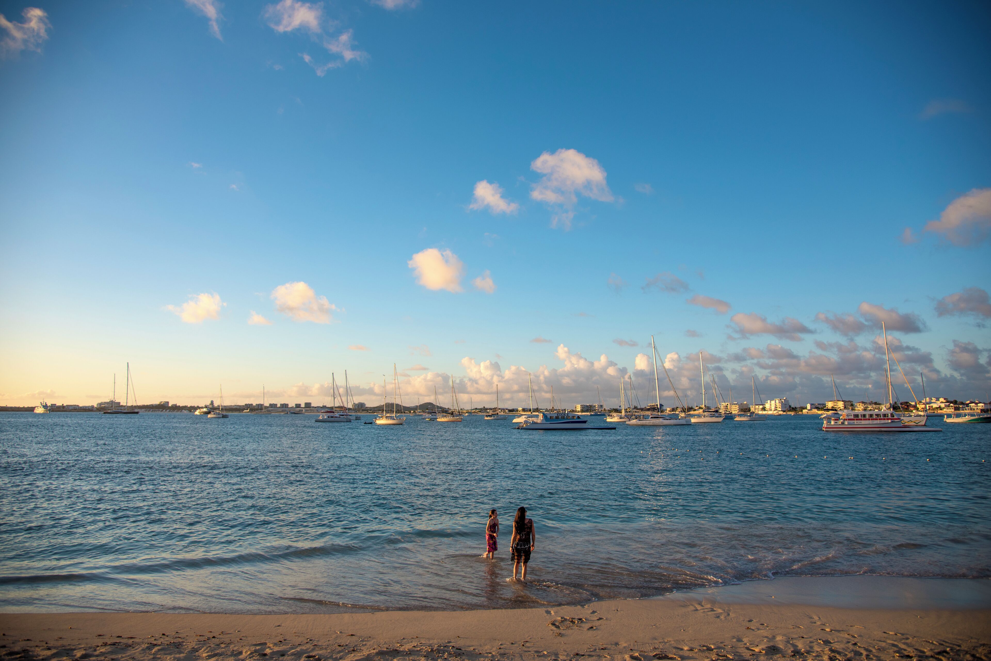 A beach with a clear sky, calm sea, and boats in the distance.