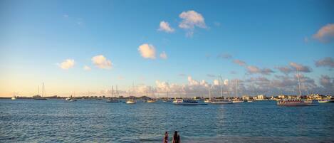 A beach with a clear sky, calm sea, and boats in the distance.