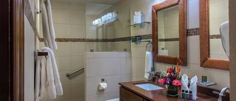 Un baño con dos lavabos, cabina de ducha de vidrio, inodoro y espejo con marco de fibras naturales.
