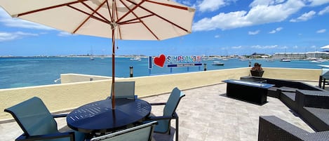 A beachside patio with outdoor seating, a large umbrella, and a view of the Simpson Bay Resort marina.