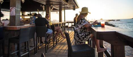 A seaside restaurant with outdoor seating, a wooden deck, and a view of the ocean.