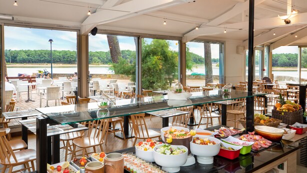 A buffet setup with various food items and a view of a lake. - SOWELL Family Pignada Plage (Soustons)