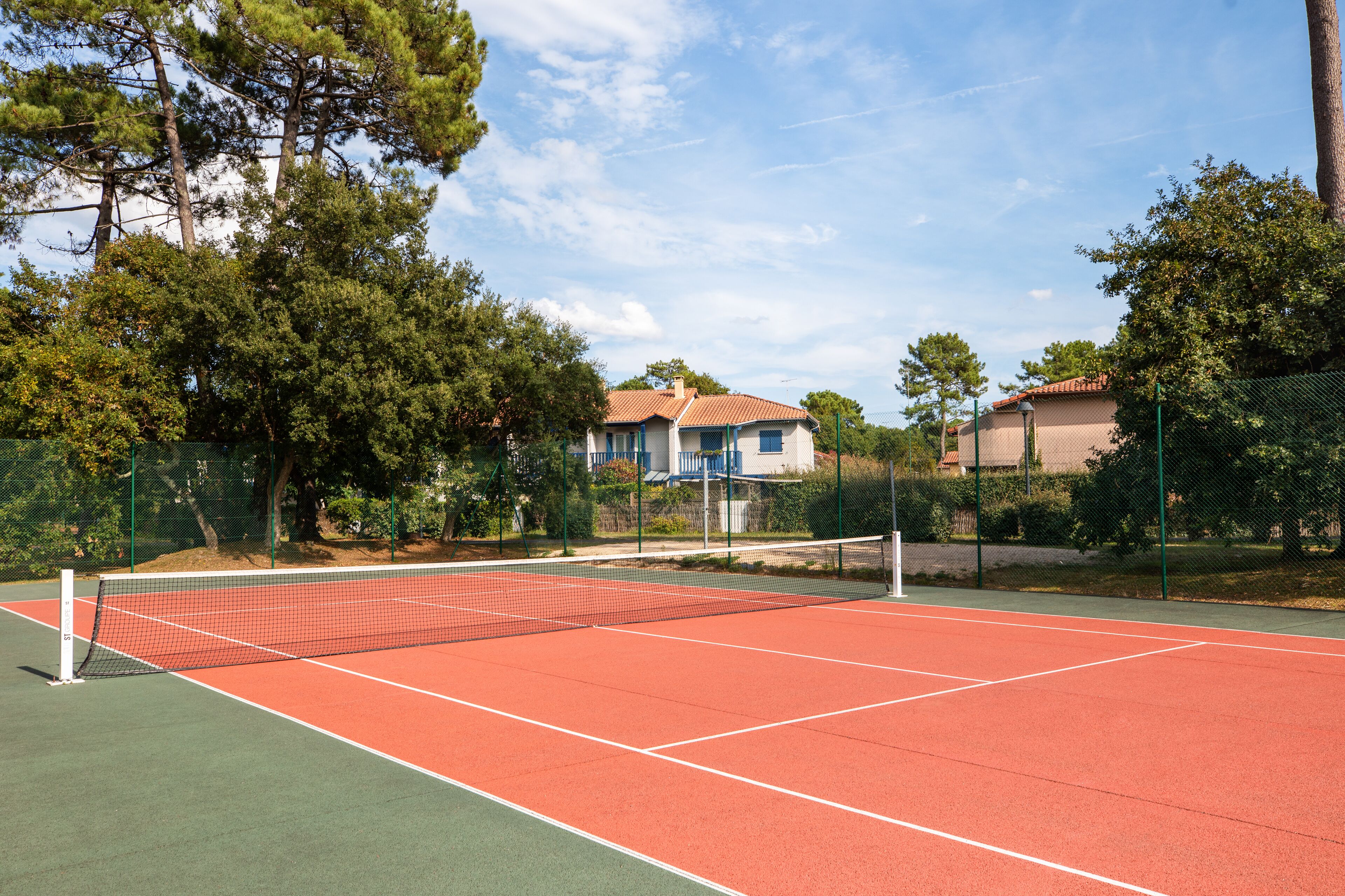 A tennis court with a net, surrounded by trees and houses.