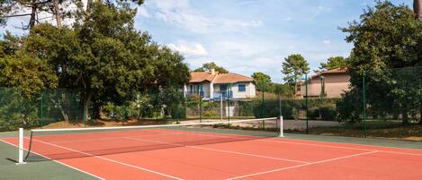 A tennis court with a net, surrounded by trees and houses.