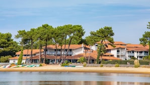 A coastal hotel with multiple buildings, a sandy beach, and boats lined up. - SOWELL Family Pignada Plage (Soustons)
