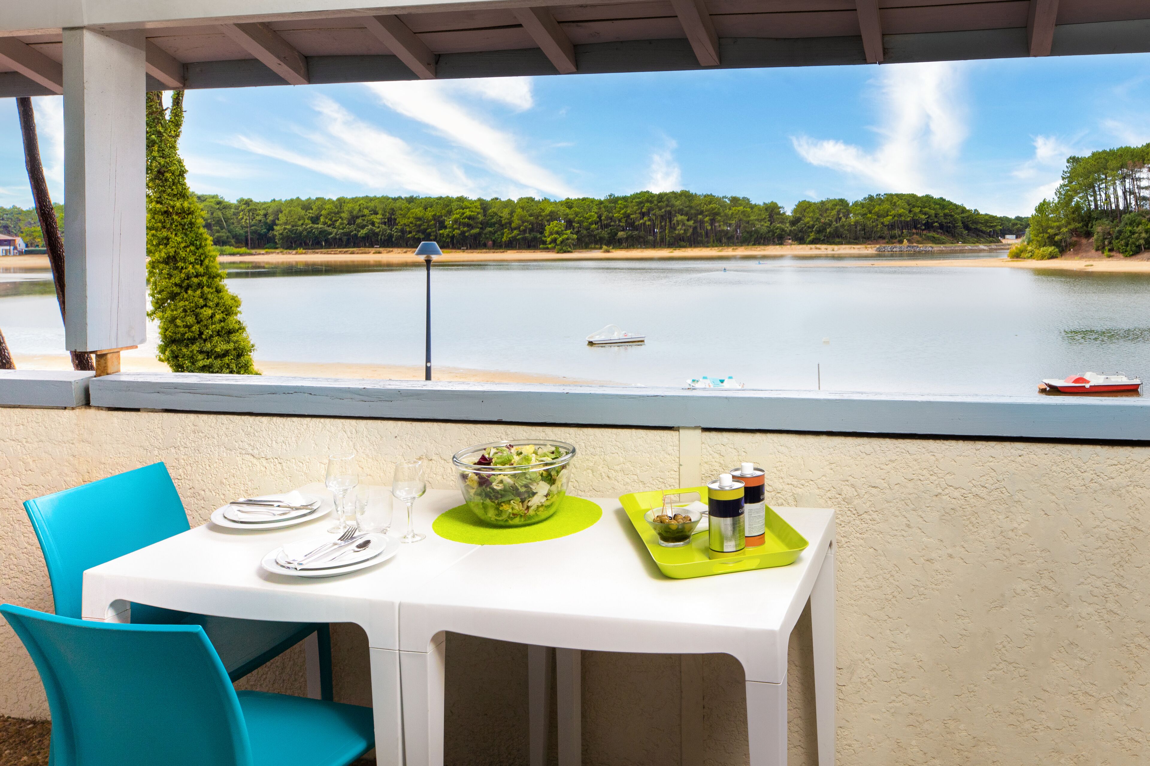 A table set for two with a clear view of a lake and a boat in the distance.