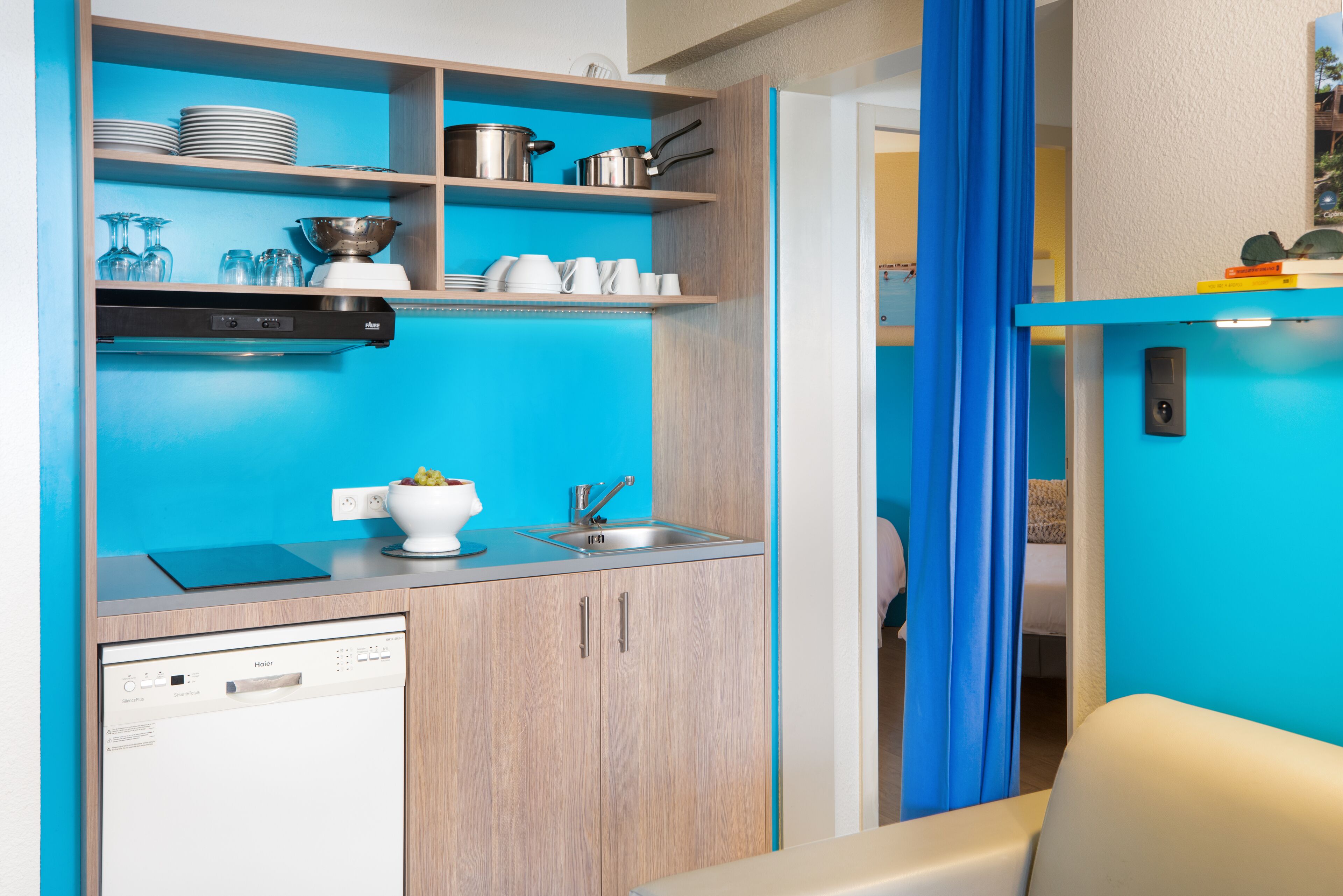A compact kitchen with a dishwasher, a sink, and various kitchenware on shelves.