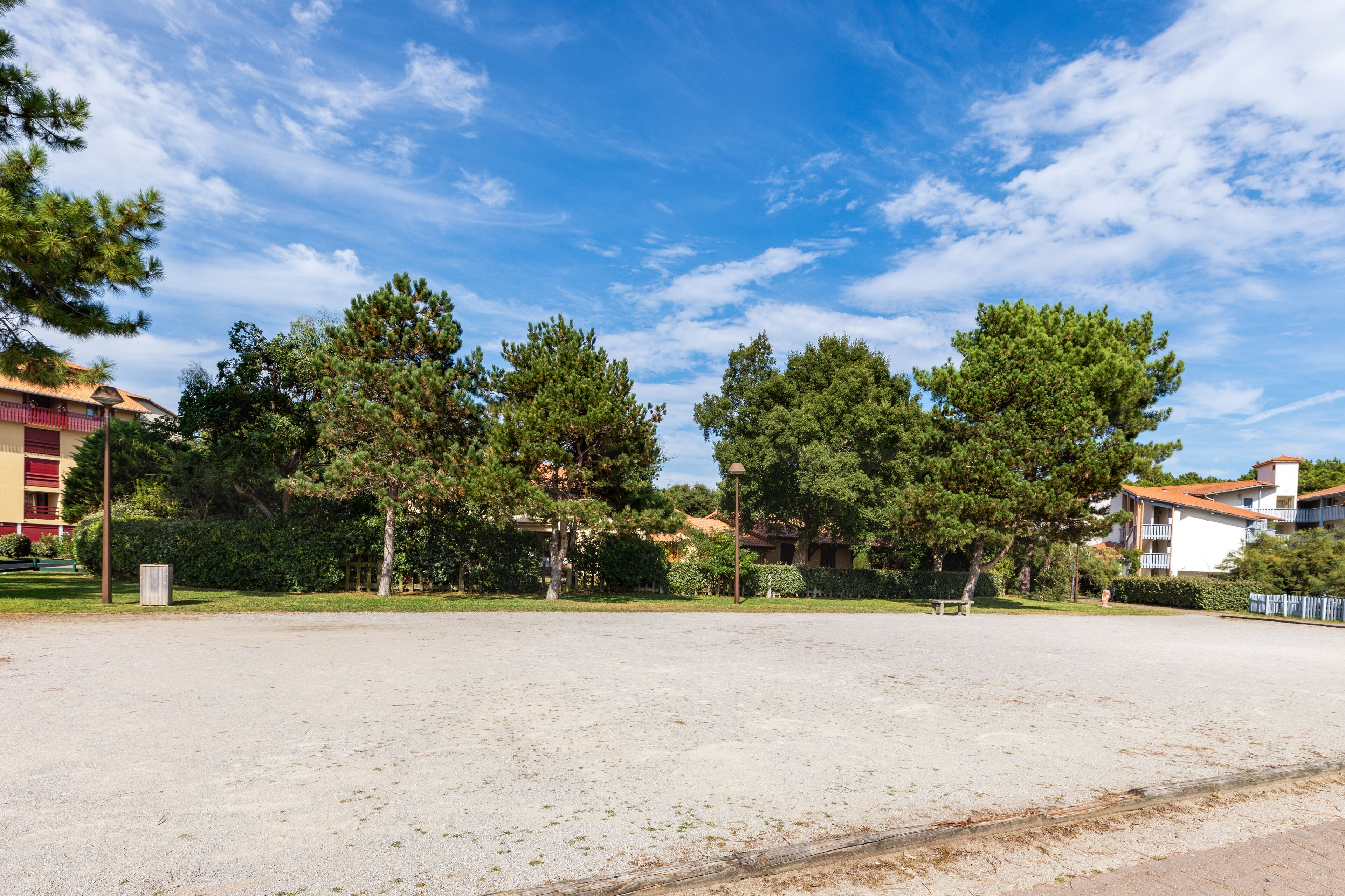 A spacious outdoor area with a gravel surface, surrounded by trees and buildings.