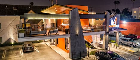 A modern hotel with a prominent 'M' logo, outdoor seating, and a parking area.
