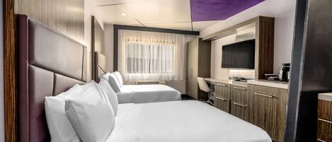 A hotel room with two beds, a desk, a flat-screen TV, and a window with sheer curtains.