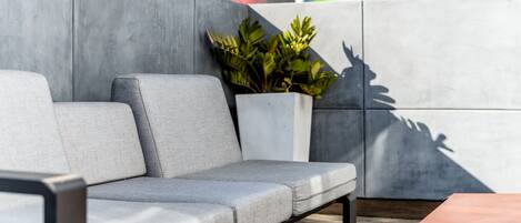 Un área de estar exterior moderna con un sofá gris, una planta en maceta y una pared de azulejos con un mural colorido.