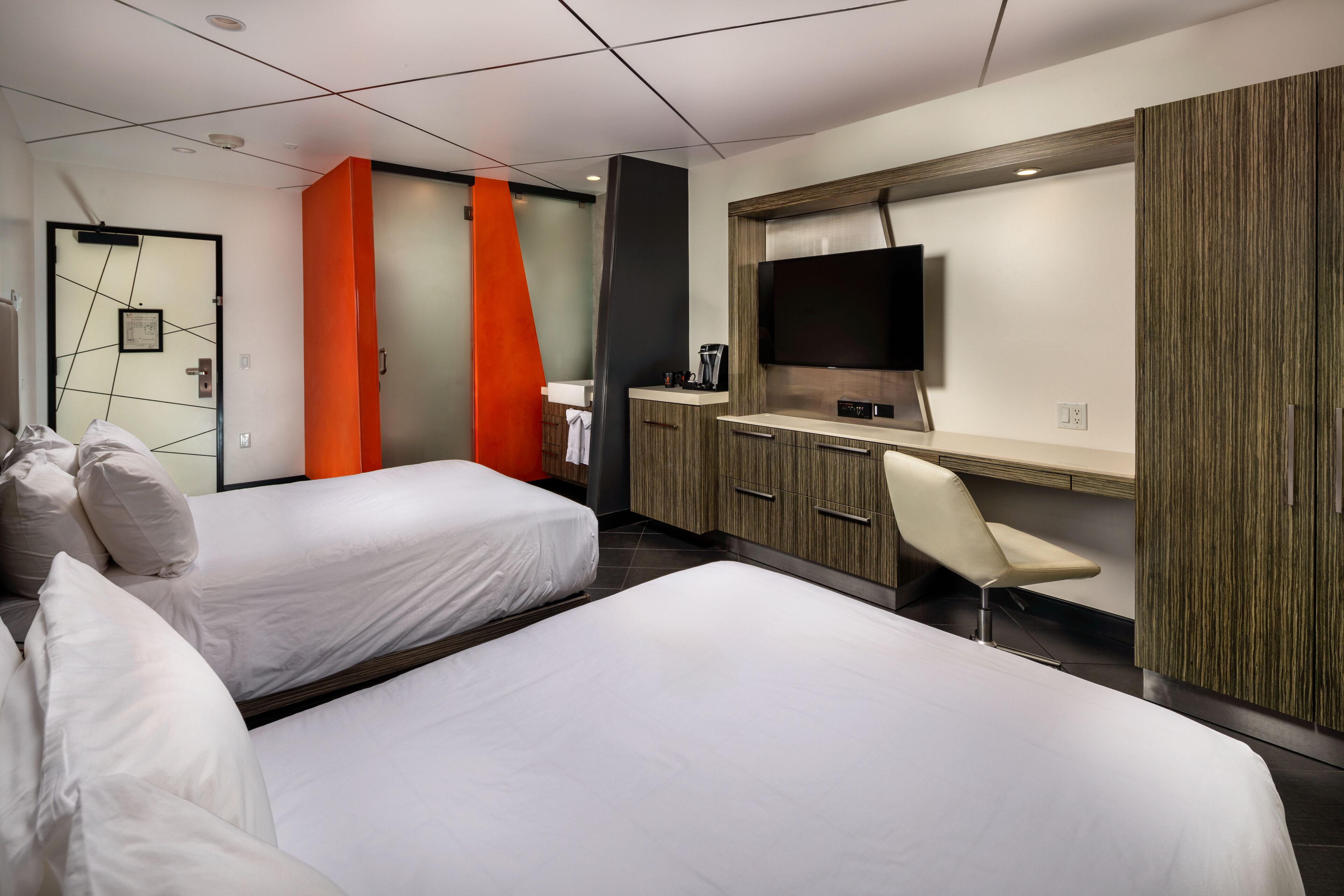 Une chambre d’hôtel moderne avec deux lits, un bureau doté d’un téléviseur à écran plat, une chaise et un mur décoratif en bois.