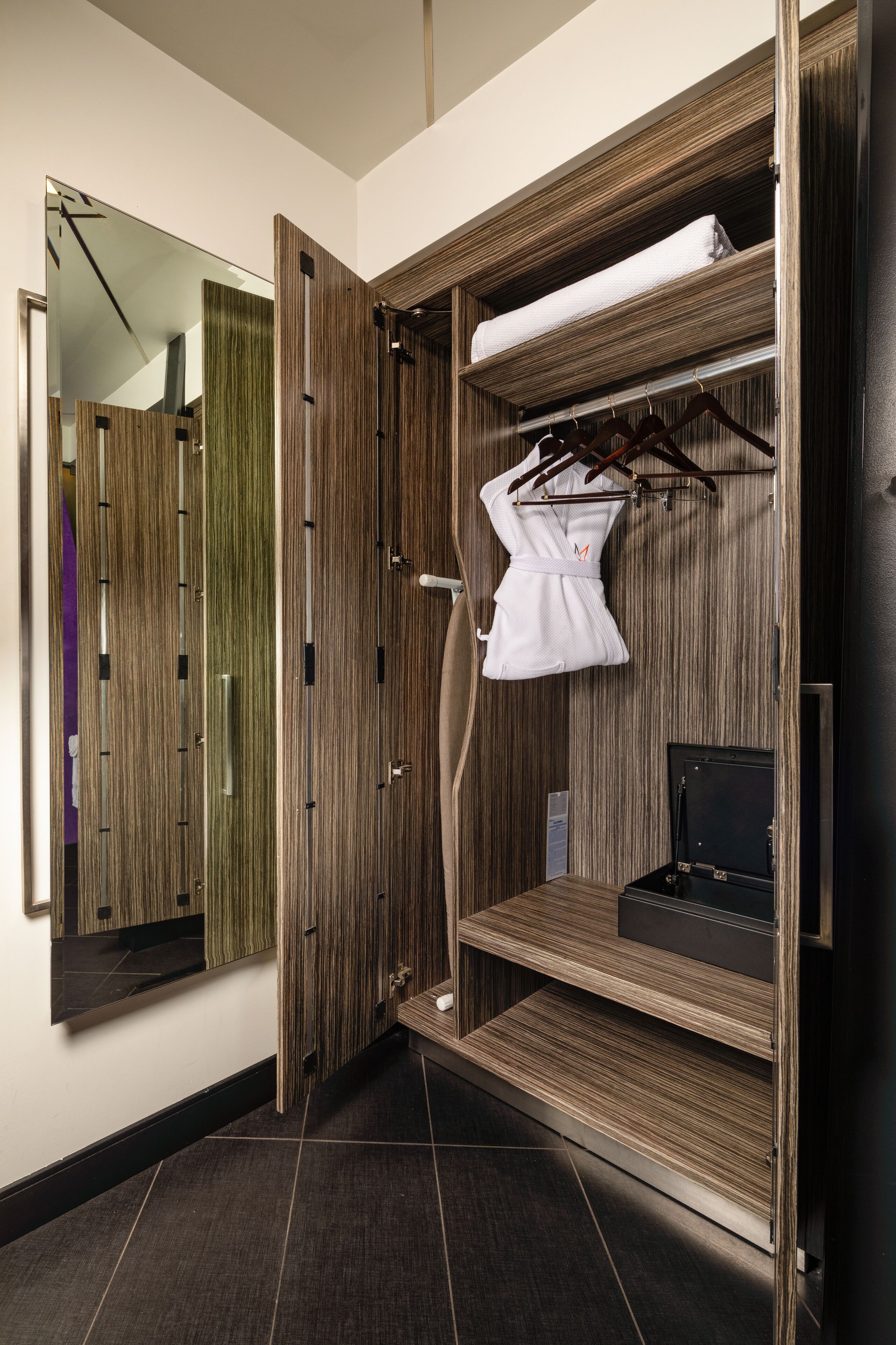 A walk-in closet with wooden paneling, a hanging robe, and a black suitcase on the lower shelf.