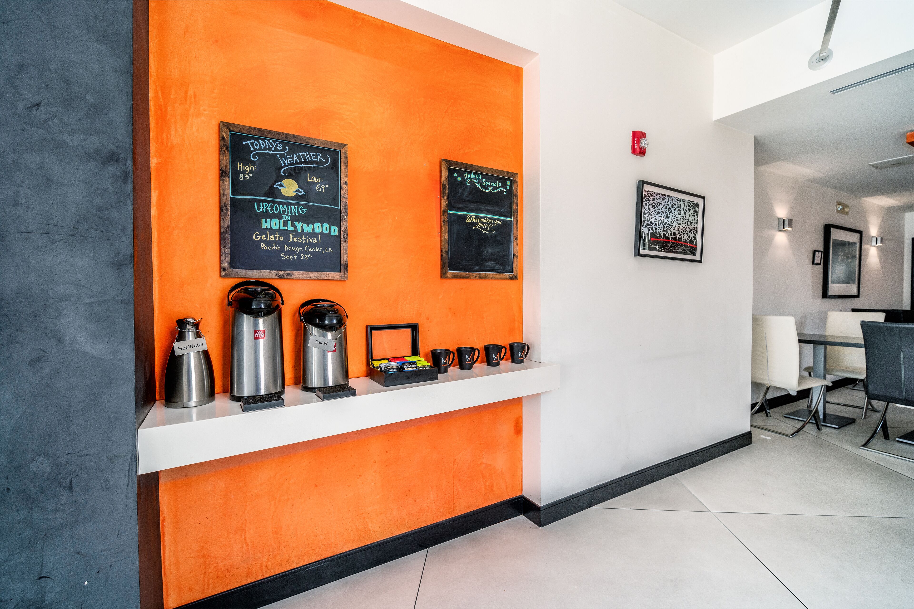 A reception area with an orange accent wall, a coffee station, and chalkboard signs displaying menu items.