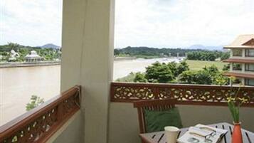A balcony with a view of a river and mountains, a wooden table with a cup and book, and a decorative railing.