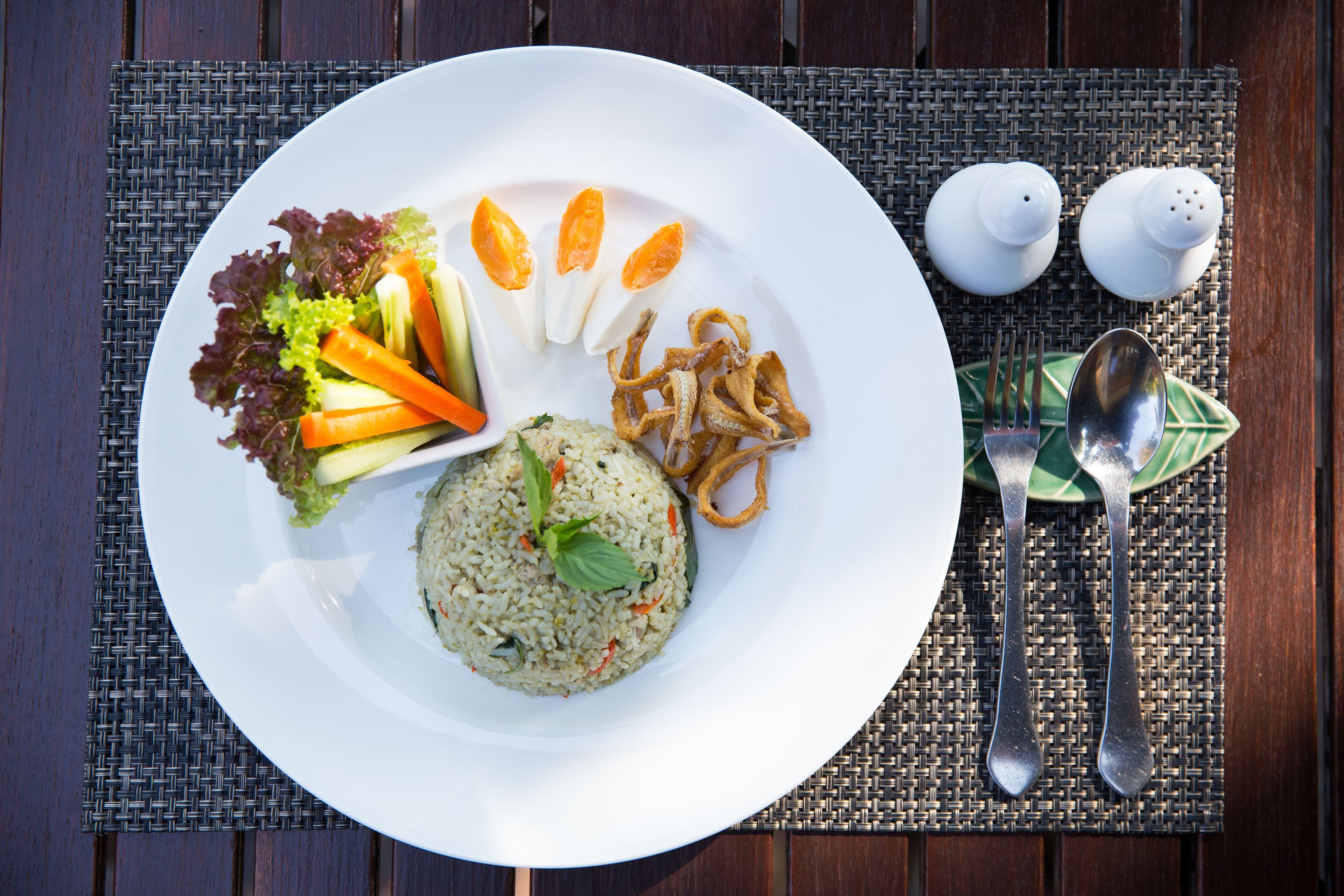 Une assiette de nourriture contenant du riz, des légumes et des aliments frits, posée sur une table recouverte d’un set de table en fibres tressées.