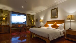 A hotel room with a large bed, a nightstand, a bedside table, a window with curtains, a sofa, and a view of the outdoors.