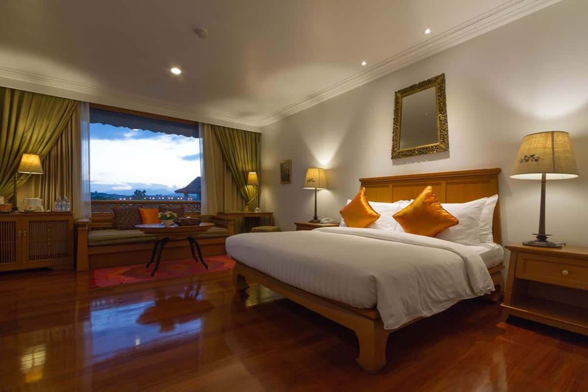 Habitación de hotel con una cama grande, una mesita de noche, un sofá y vistas al exterior.