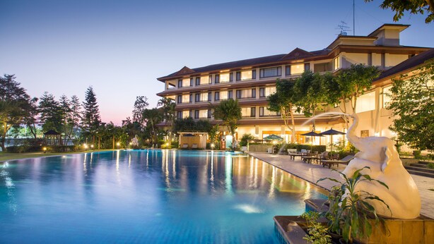 A hotel with a swimming pool, outdoor seating, and a large building with multiple floors.