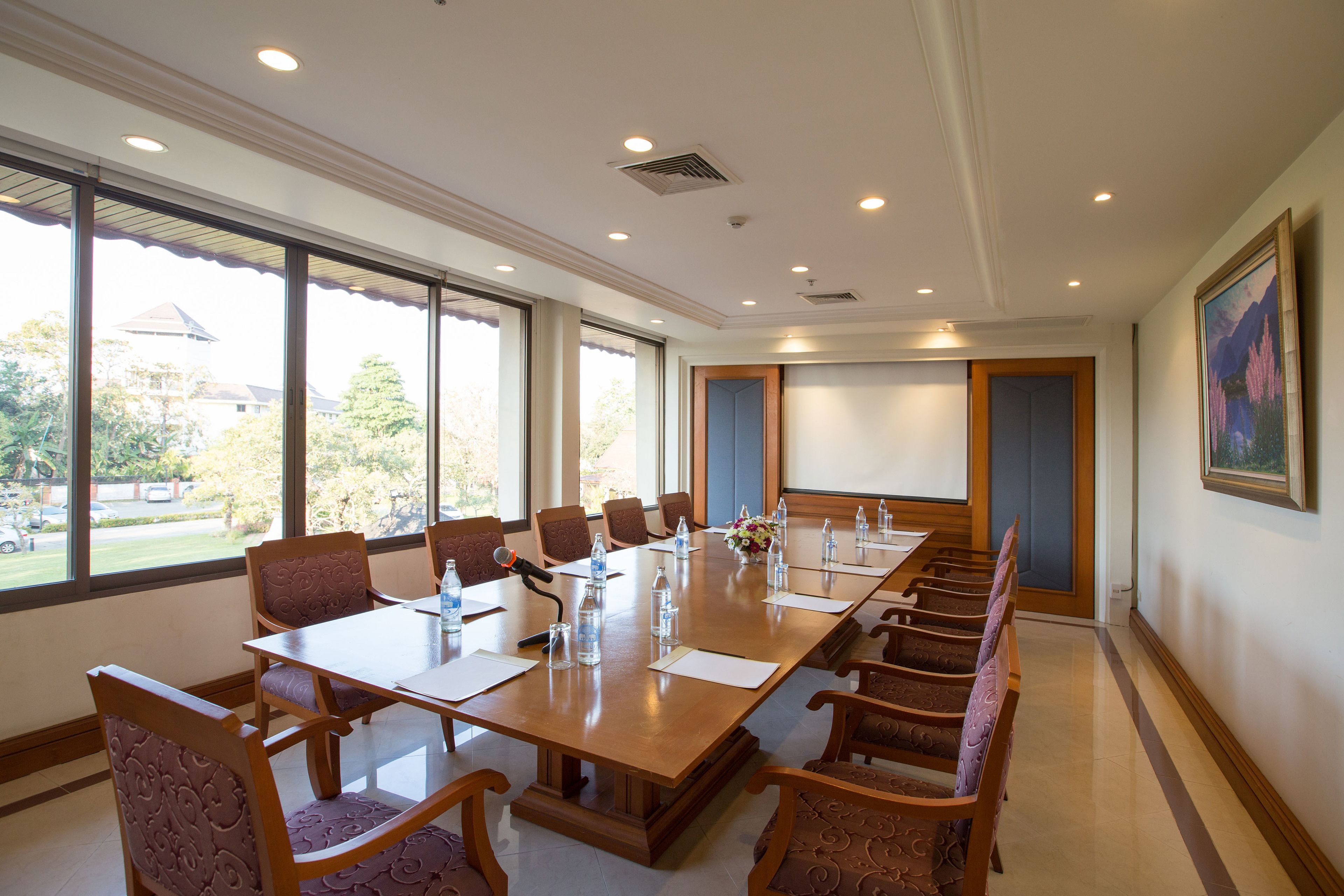Un salón de conferencias con una larga mesa, sillas y una pantalla para proyector.
