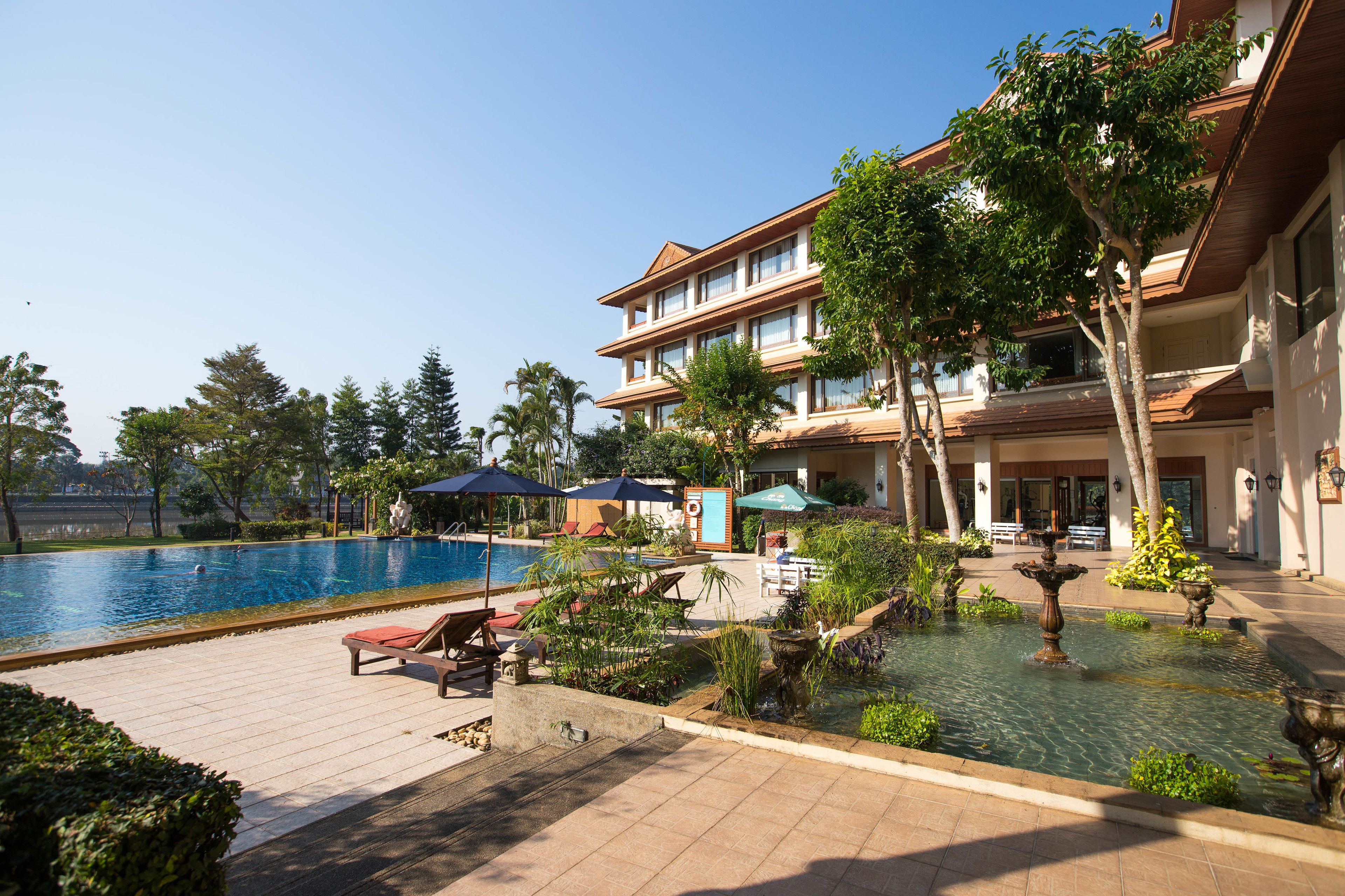 Een hotel met een zwembad, terras en een fontein.