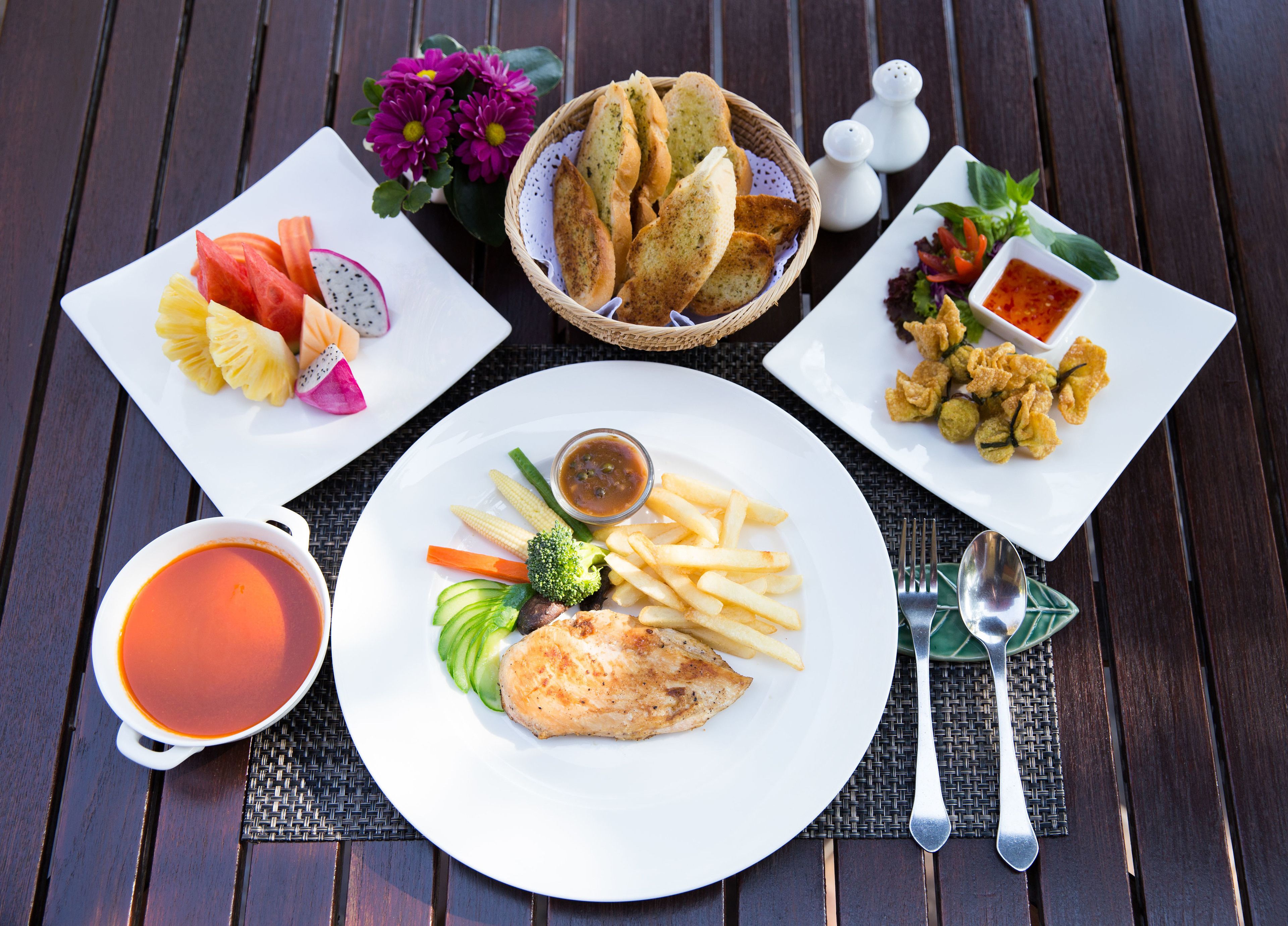 A table with a variety of dishes including a plate of fish, fries, and vegetables, a basket of bread, and a cup of soup.