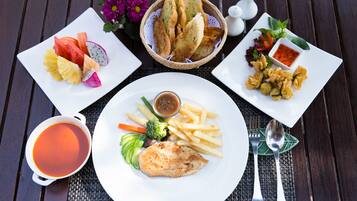 A table with a variety of dishes including a plate of fish, fries, and vegetables, a basket of bread, and a cup of soup.