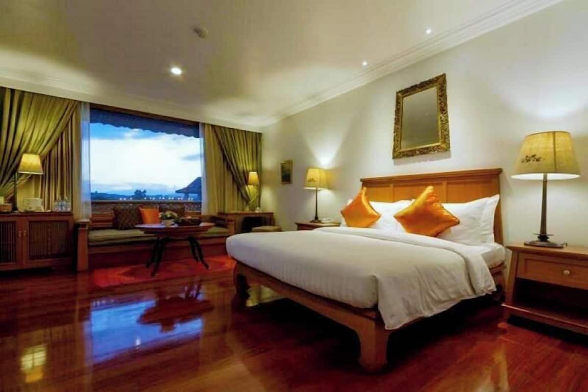 Habitación de hotel con una cama grande, una mesita de noche, un sofá y vistas al exterior.