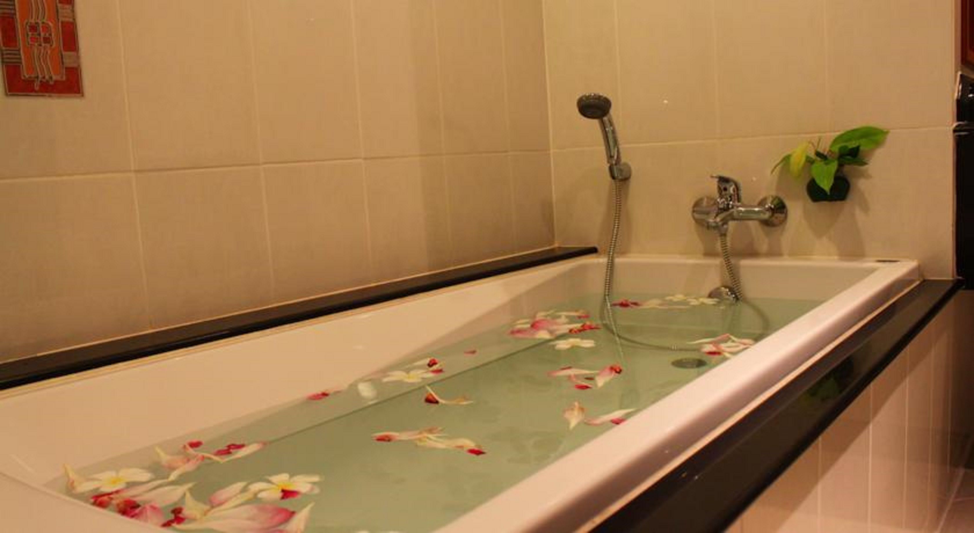 Una bañera con pétalos de flores flotando en el agua, un cabezal de ducha y una planta en maceta.