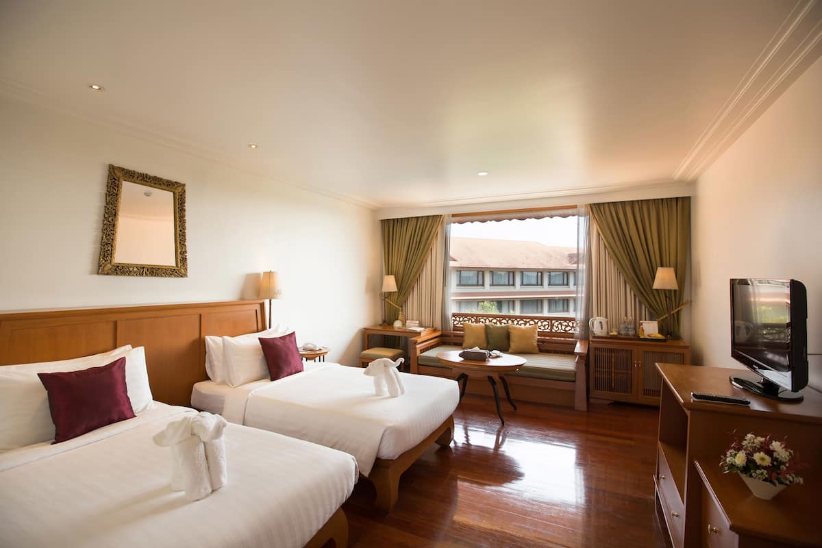 Habitación de hotel con dos camas, televisión, escritorio y ventana con cortinas.