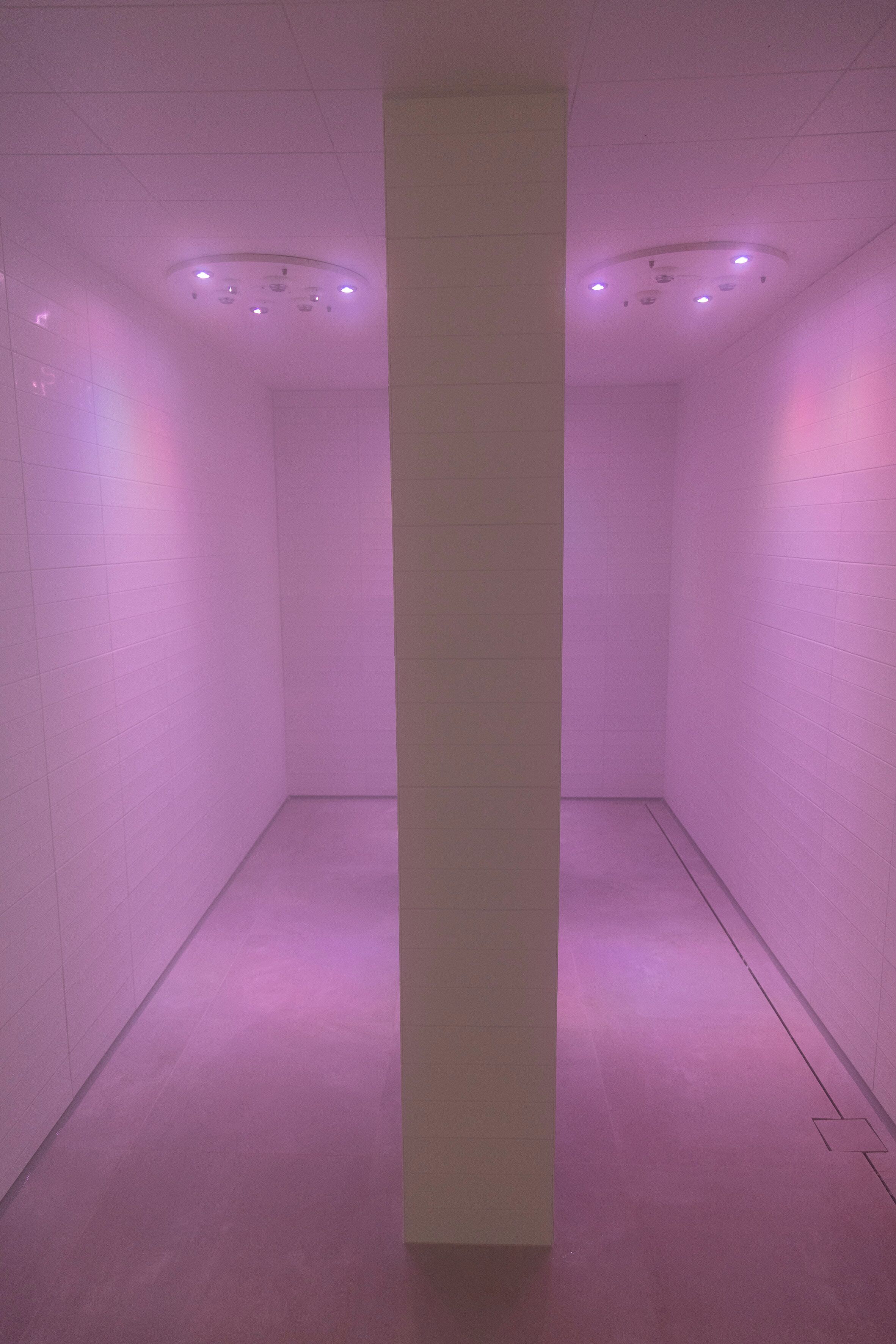 A narrow hallway with white tiled walls and a central pillar.