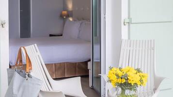 Une pièce avec un lit, une table ornée d’un vase de fleurs et une chaise sur laquelle est posé un sac.