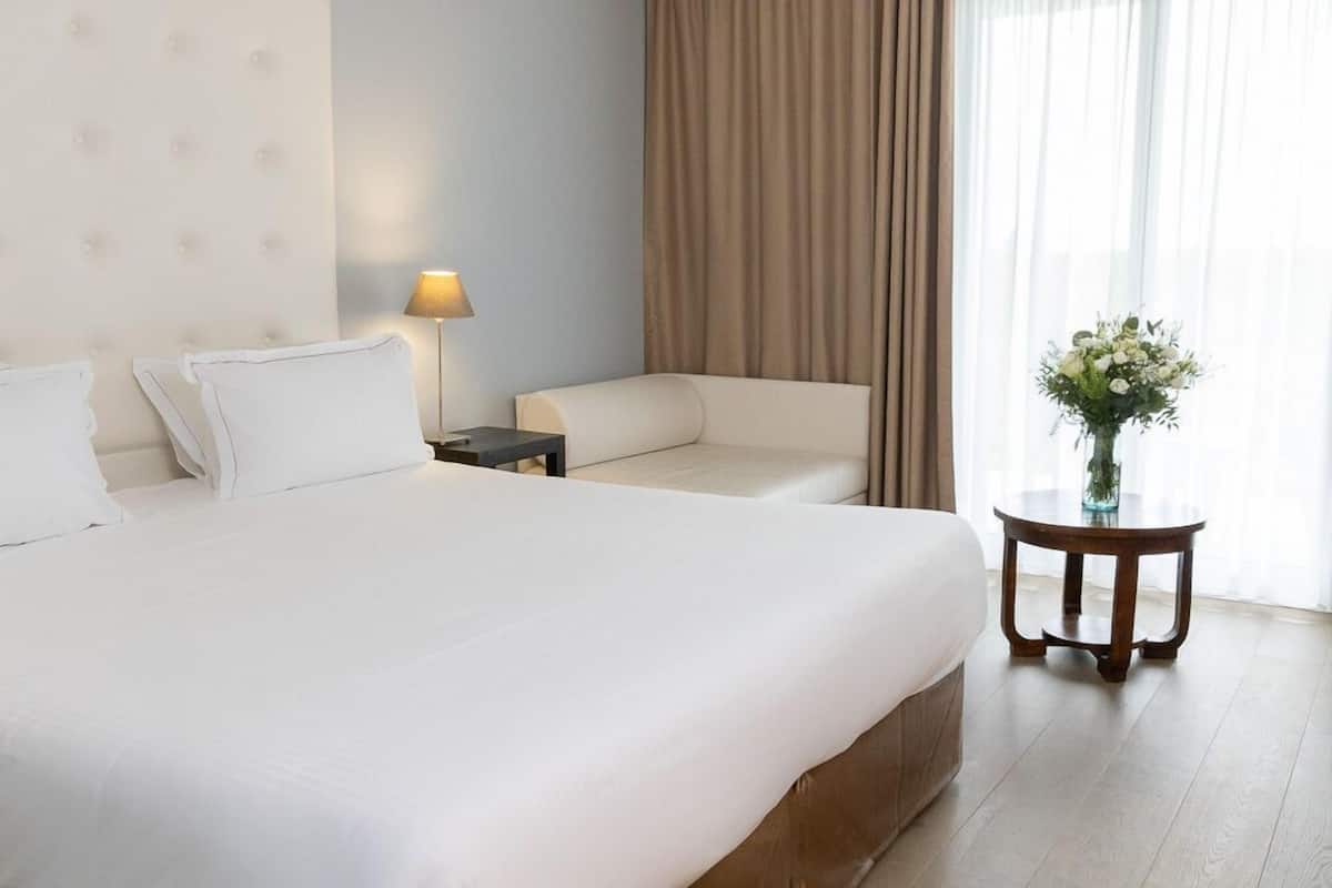 Une chambre d’hôtel avec un grand lit, une table de chevet, un canapé et une petite table sur laquelle est posé un vase de fleurs.