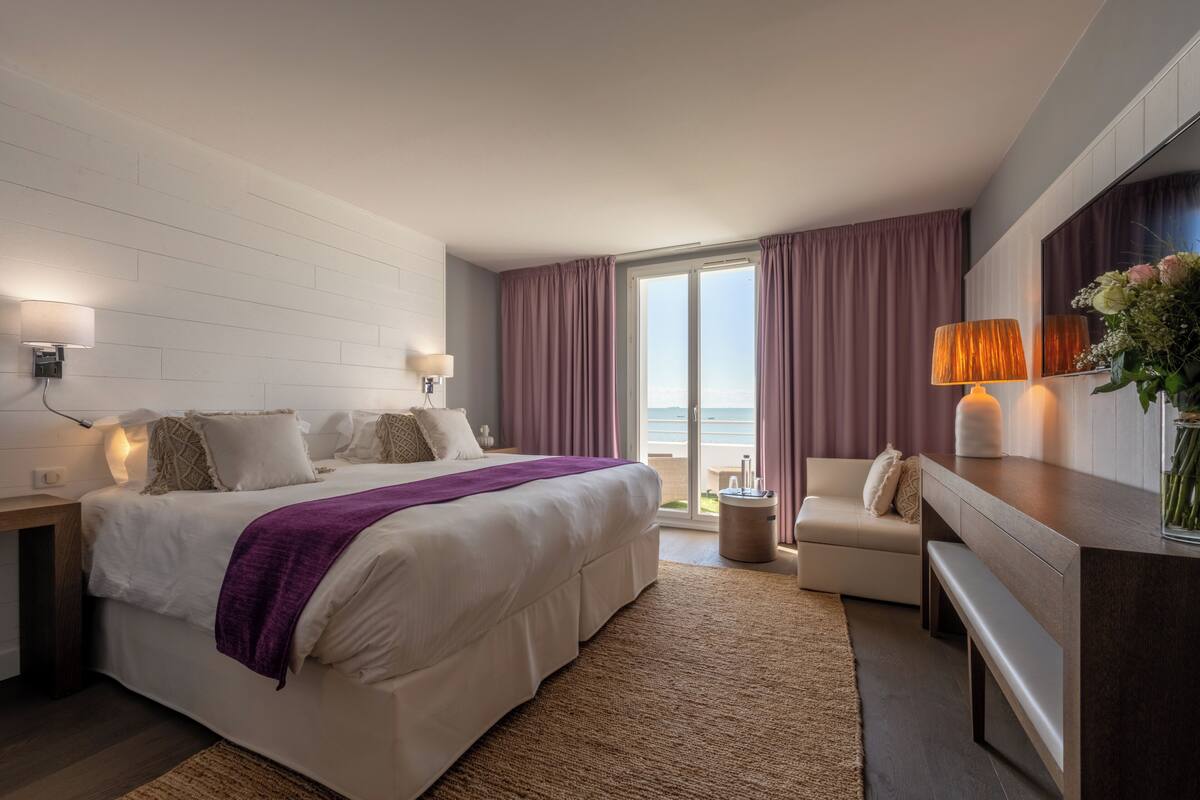 Une chambre d’hôtel moderne dotée d’un grand lit, d’un coin salon, d’un bureau et offrant une vue sur l’extérieur.